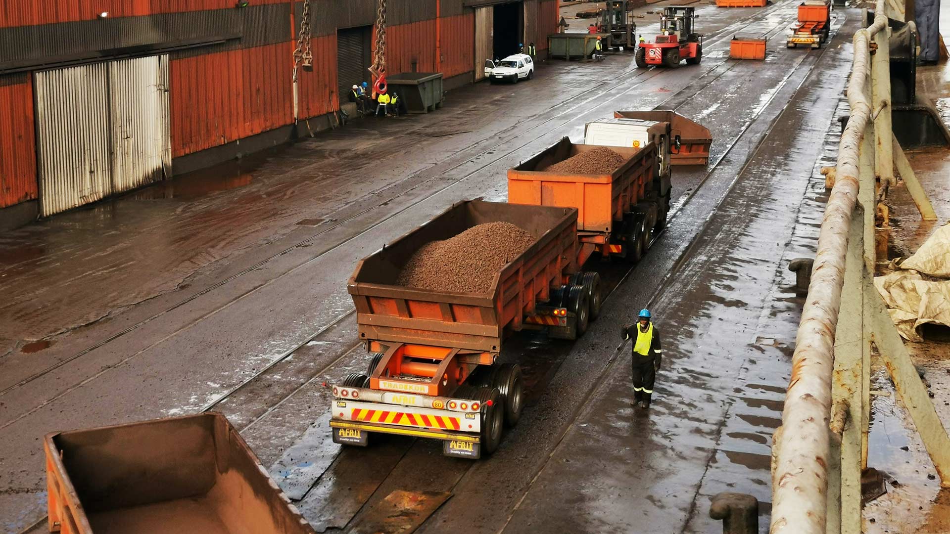 orange dump trucks loaded with bulk material are parked on a wet industrial site