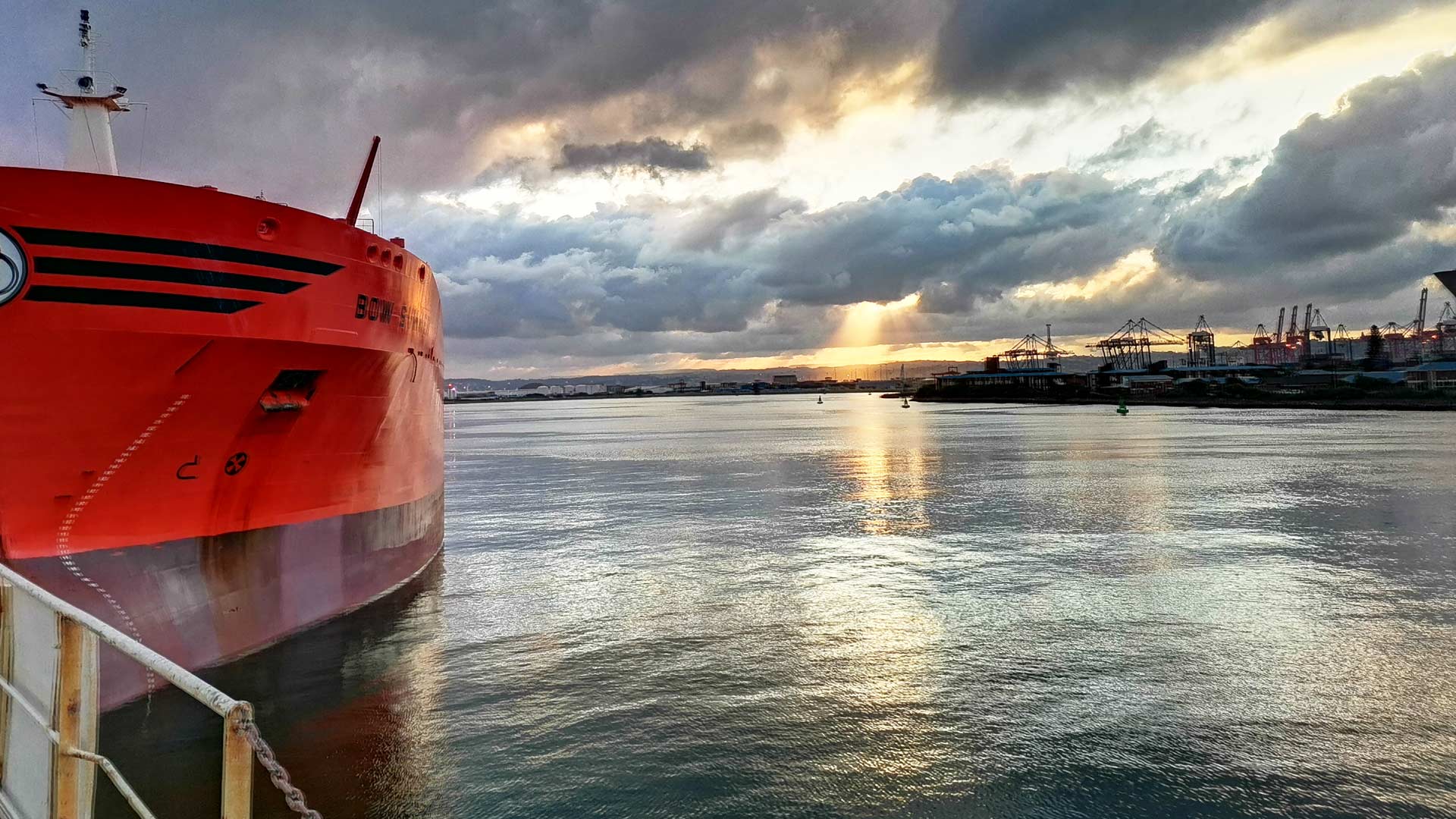 red ship docked near a calm harbour at sunset