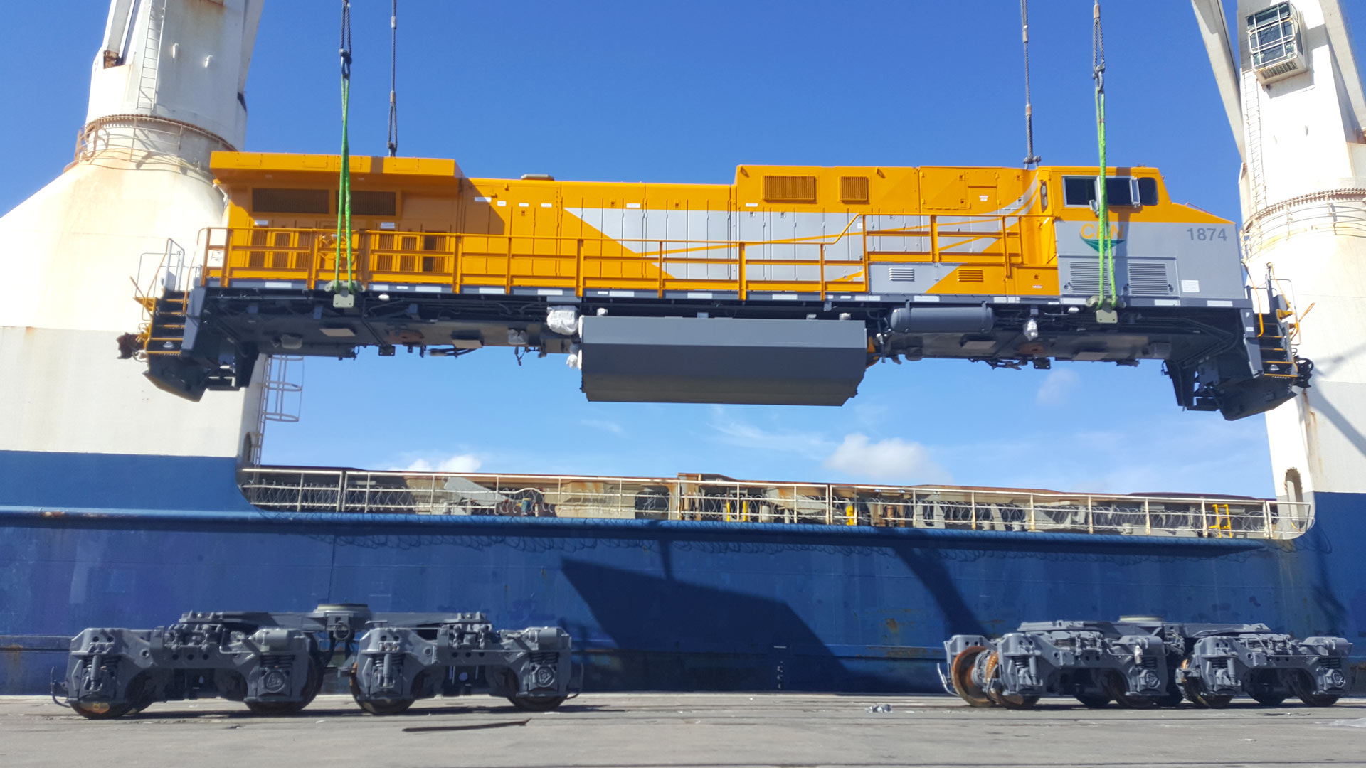 heavy lift operation loading a yellow locomotive onto a cargo ship at a commercial port using ship cranes
