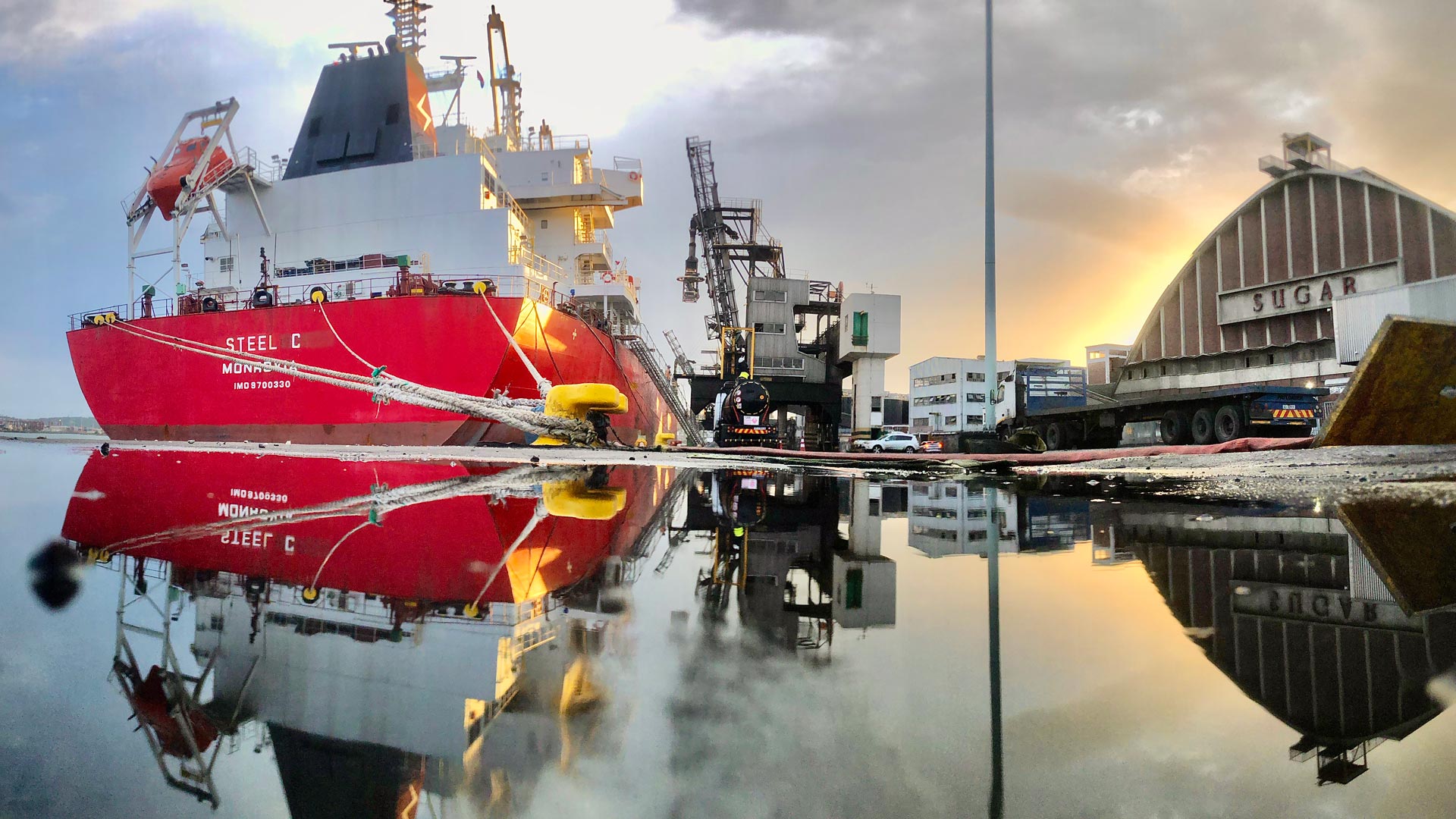 large red cargo ship docked at a port near a warehouse